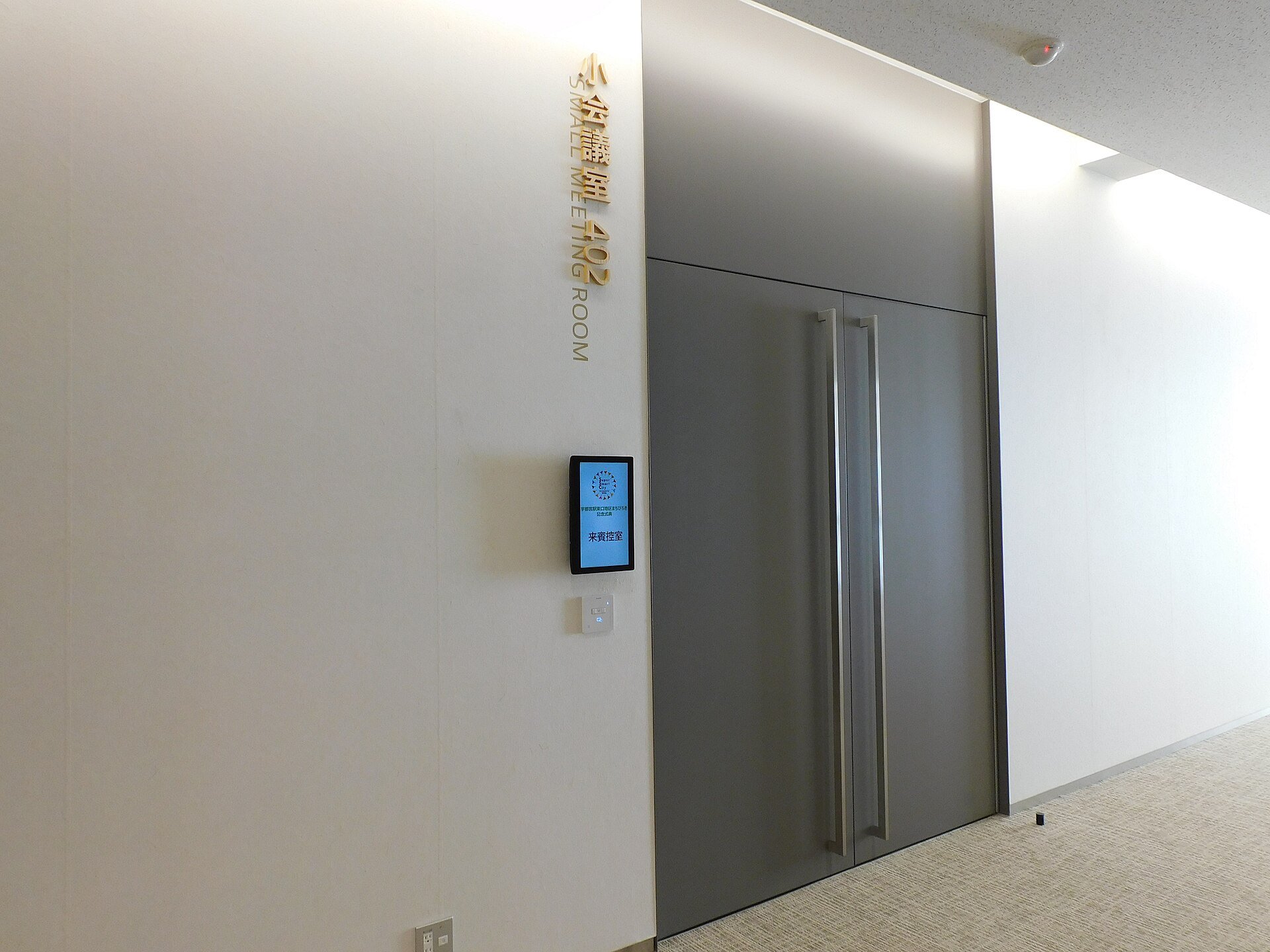 Porta cinza de sala de reunião com placa dourada e tela